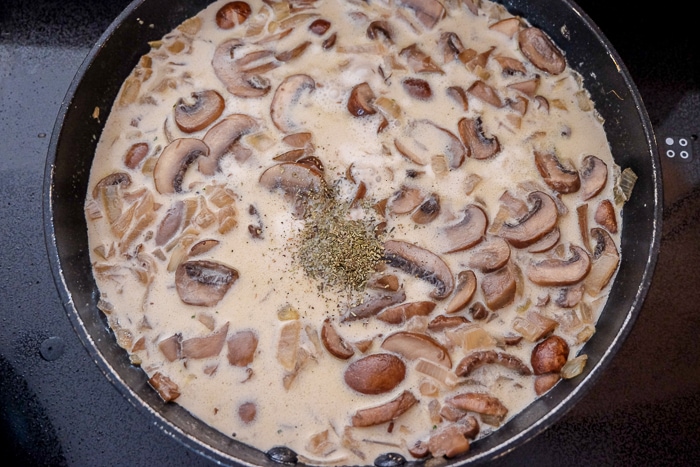 mushroom sauce with green dry spice in black frying pan on stove top