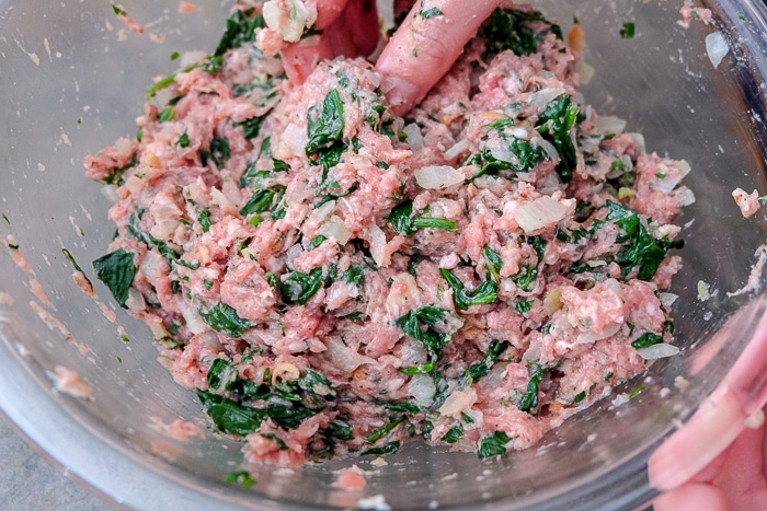 meat blend with spinach in clear glass bowl mixed with hands