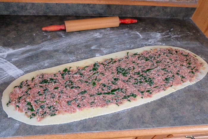 raw meat blend spread on rolled dough on counter top