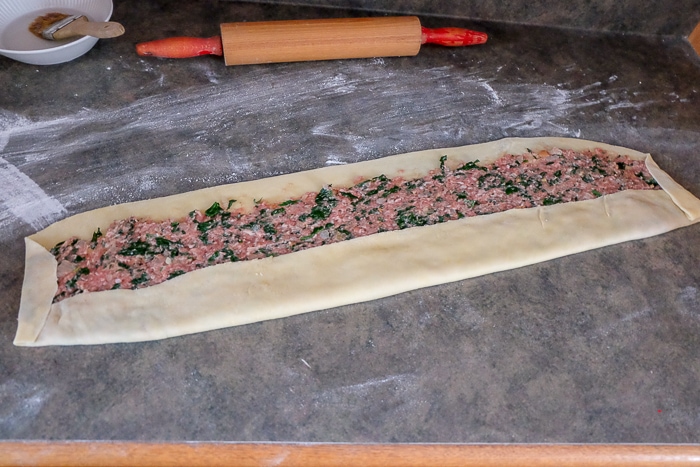 folded dough with raw meat spread inside with rolling pin behind