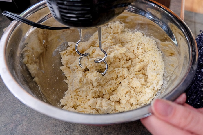 hand mixer with dough hooks blending dough in silver bowl