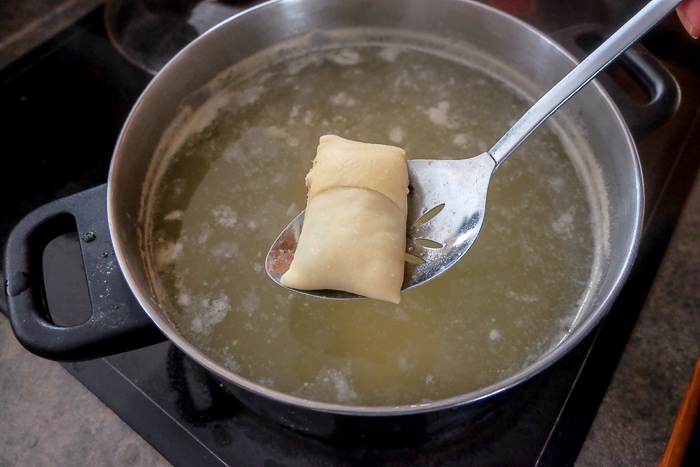 dunking maultaschen pasta into boiling water with straining spoon