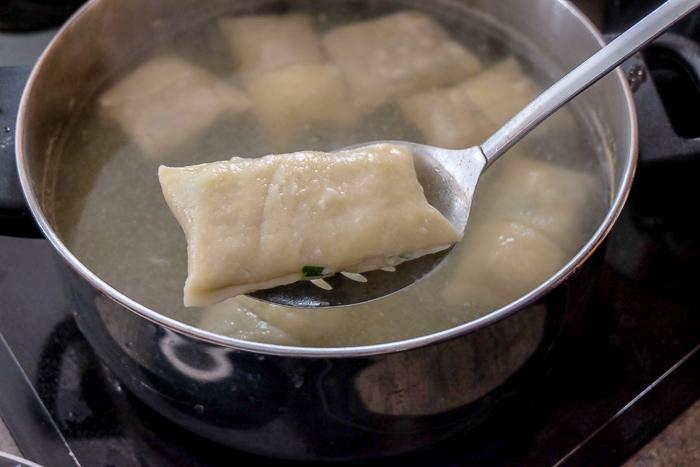 lifting maultaschen from silver pot on stove with straining spoon