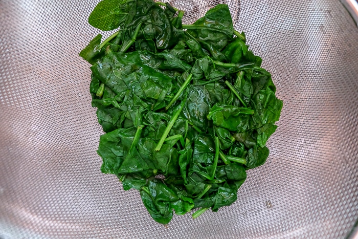 cooked spinach in strainer in sink