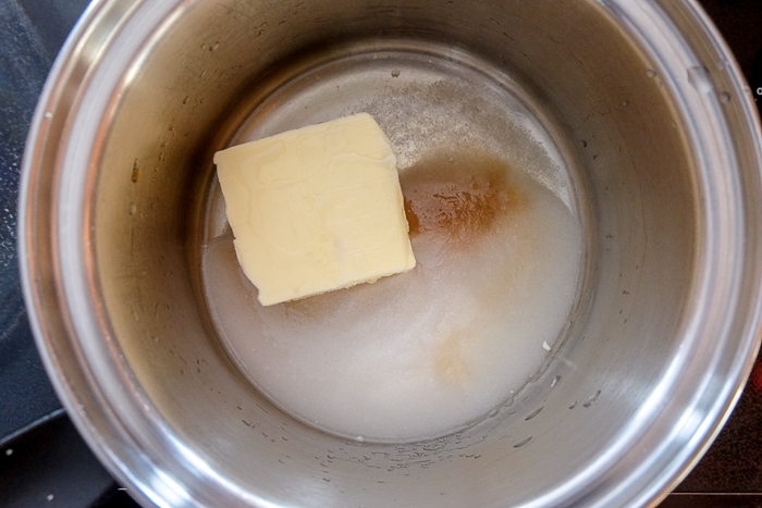 chunk of butter melting in silver pot on stove with sugar