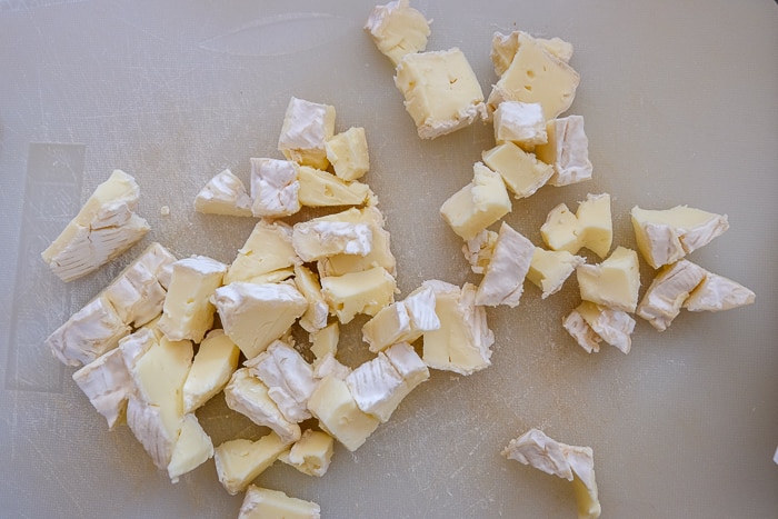 camembert cheese cut up into pieces on cutting board