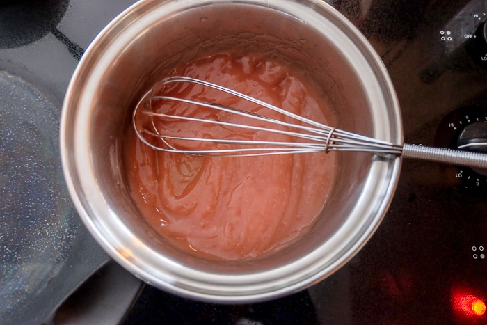 thickened sauce in silver pot with whisk on stove