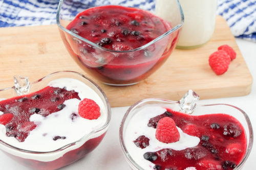 bowls of red berries with white cream on top on white counter or wooden board