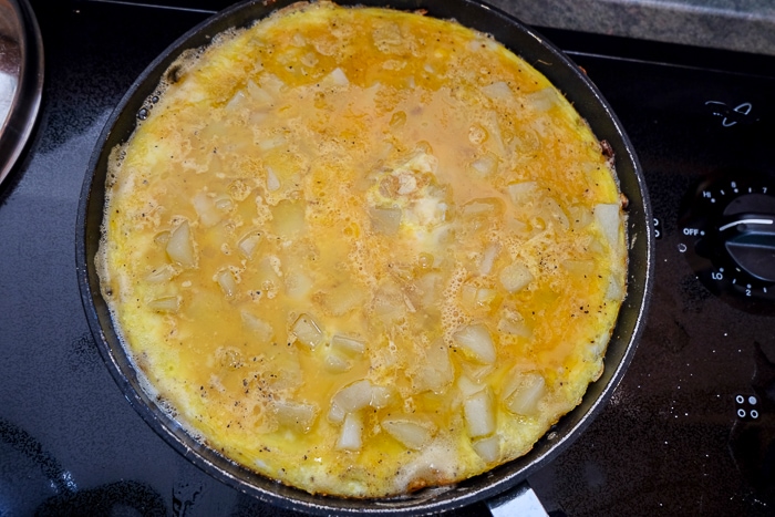 raw spanish omelette cooking in black frying pan on stove