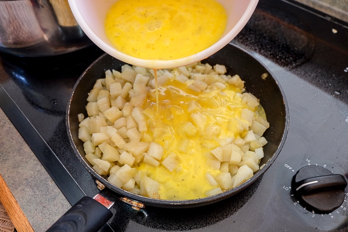 pouring scrambled egg into pan of cooked potatoes on stove top