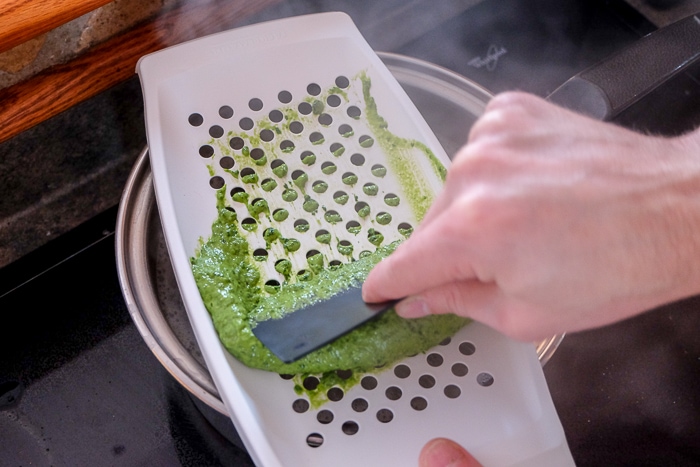 hand scraping green spinach spaetzle batter on white spaetzle grater