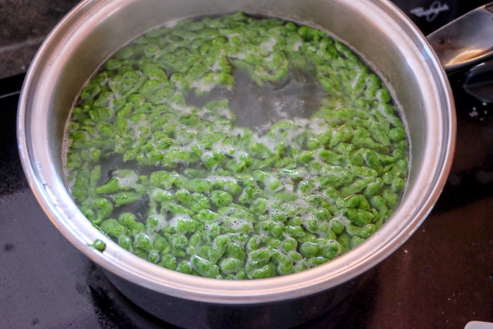 boiling water in silver pot with green spinach spaetzle floating to the top