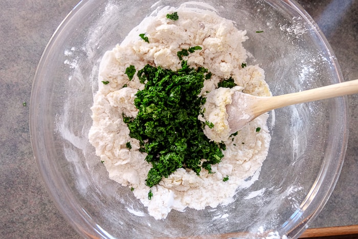 green chopped spinach in flour mix in clear bowl with wooden spoon