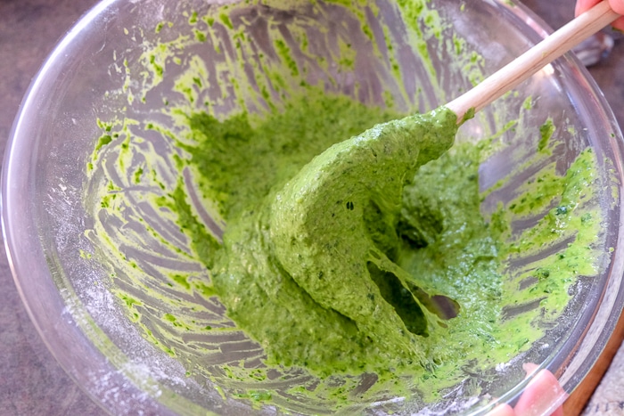 green spinach spaetzle batter in clear bowl with wooden spoon