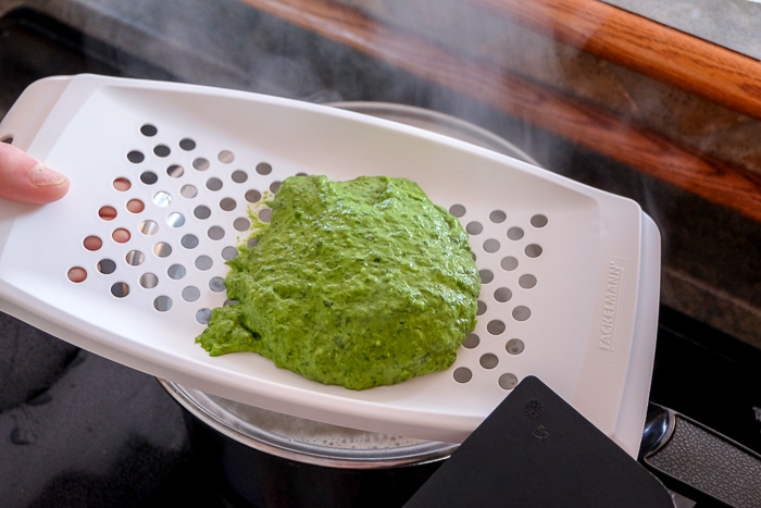 green spinach spaetzle dough on spaetzle maker over boiling pot