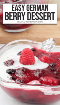 Red berry dessert in clear bowl with cold whipping cream and fresh raspberry on top plus text overlay saying "easy german berry dessert"