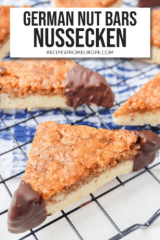 Nut bars cut into triangles with chocolate dipped corners on black cooling tray with text overlay saying "German nut bars Nussecken"