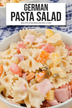 bow tie pasta salad with cut up pickles, ham and bell peppers in white bowl with text overlay saying "german pasta salad"