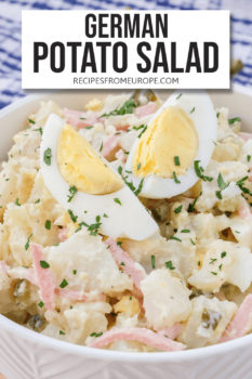 creamy potato salad in white bowl with sliced egg and chopped parsley on top plus text overlay saying "german potato salad"