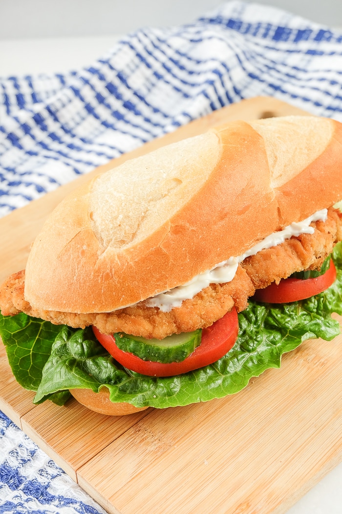 german schnitzel on bun with lettuce and tomato on wooden board