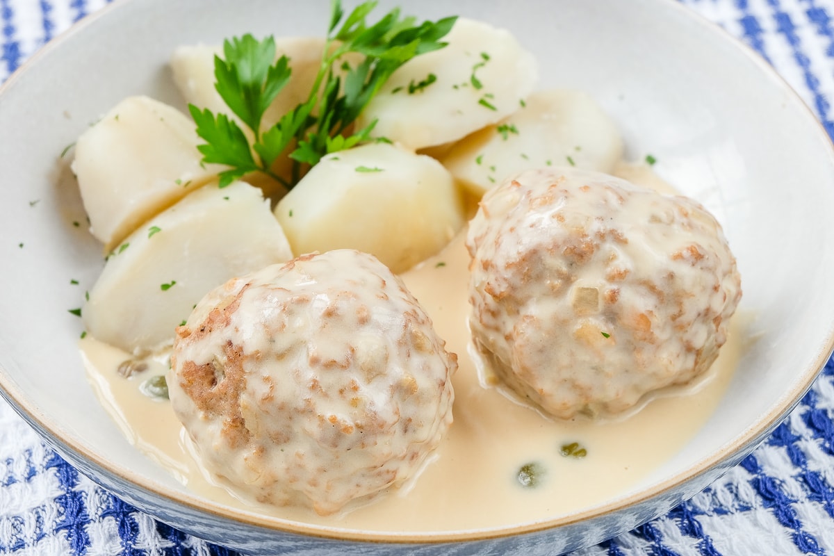 two meatballs in a dish with potatoes and parsley on blue cloth
