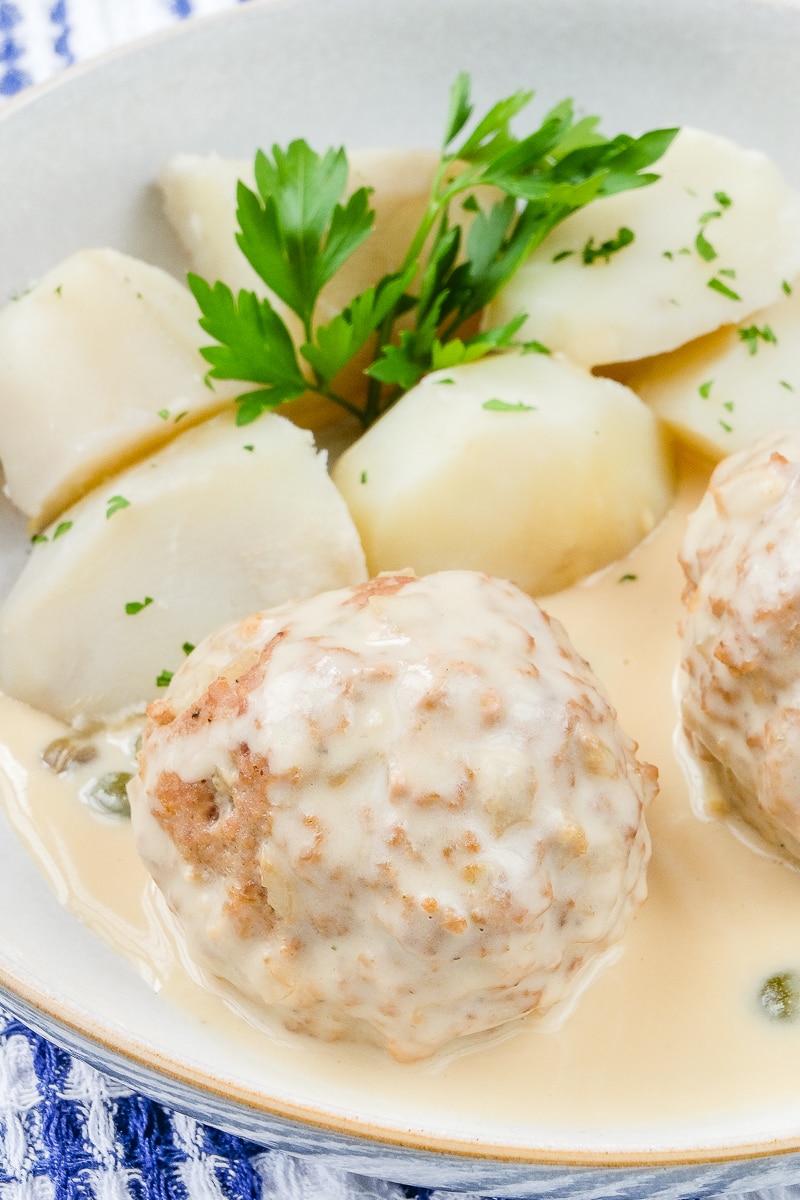 german meatball covered in creamy gravy in bowl with potatoes and parsley