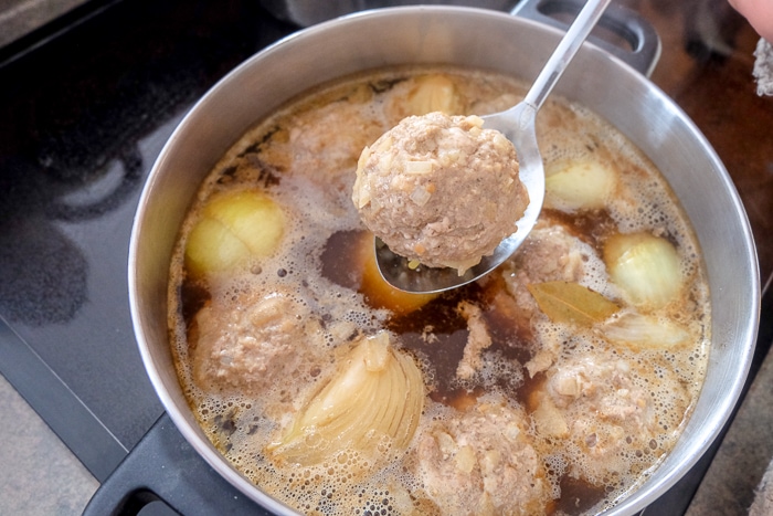 german meatball on straining spoon lifted from boiling pot on stove