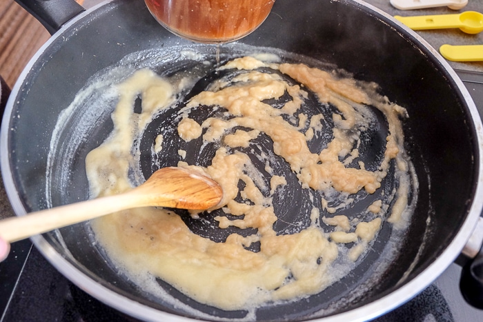 broth pouring into flour roux in large black sauce pan