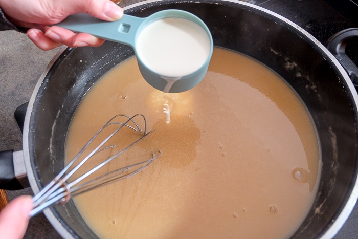pouring milk into brown gravy in sauce pan on stove with whisk