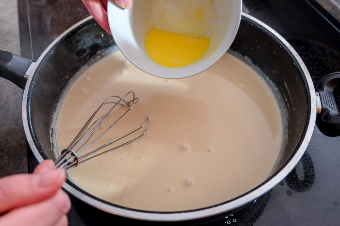 egg pouring into brown gravy in large sauce pan with whisk