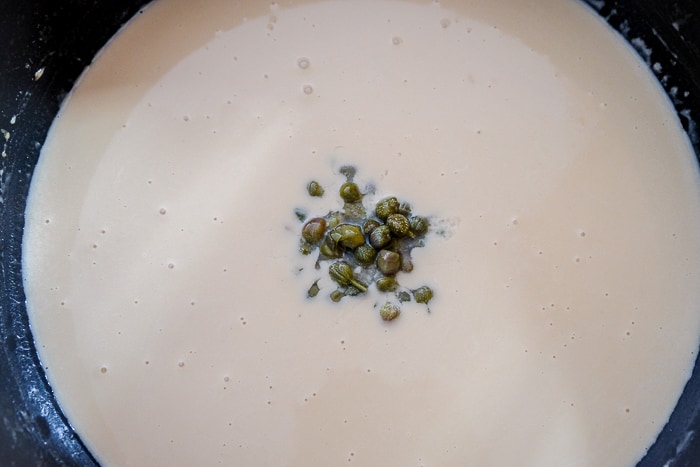 green capers placed in brown gravy in large sauce pan