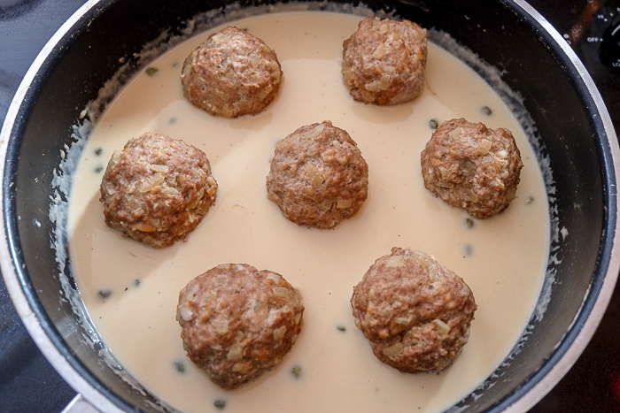 german meatballs sitting in cream sauce in large black sauce pan