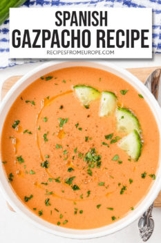 cold orange soup in white bowl with chopped cucumber and chopped parsley on top plus text overlay saying "Spanish gazpacho recipe"