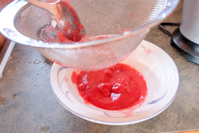 raspberries pushed through strainer into bowl below on counter