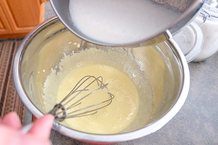 pouring milk into thick egg mixture in bowl with whisk