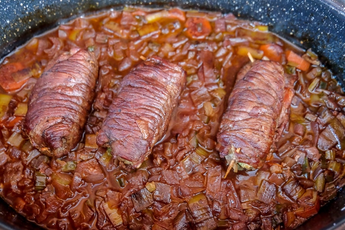 cooked rolled beef rouladen on cooked vegetables in roasting pan