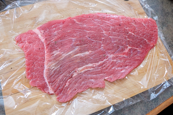 piece of beef on cling wrap with salt and pepper on top