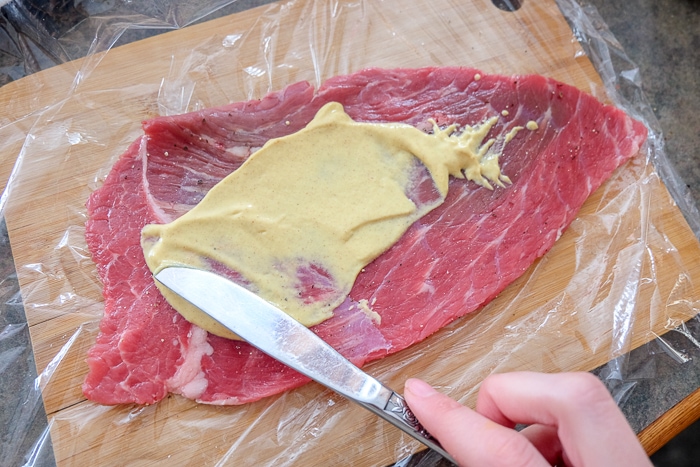 beef spread with yellow mustard with knife on wooden board