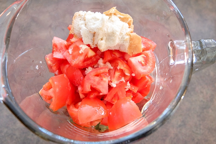 chopped tomatoes and bread in glass blender on counter