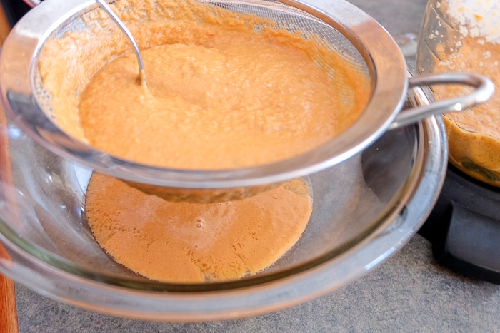 sifting gazpacho through metal strainer into bowl