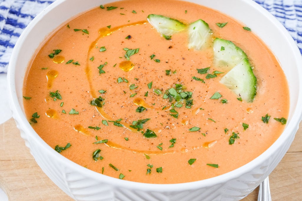 orange gazpacho soup in white bowl with cucumber and oil on top