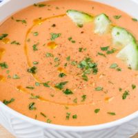 orange gazpacho soup in white bowl with cucumber and oil on top