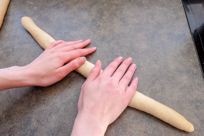 hands rolling sausage of sweet bread dough on counter top