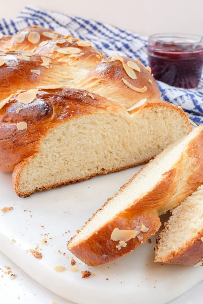 loaf of braided sweet bread on white marble with jam behind