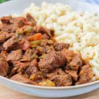 hungarian beef stew in bowl on wooden board with nokedli noodles