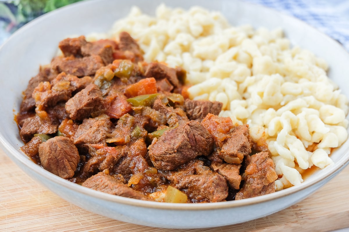 hungarian beef stew in bowl on wooden board with nokedli noodles