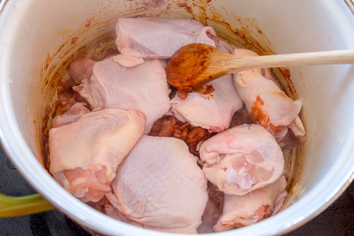 raw chicken thighs in pot on stove with wooden spoon