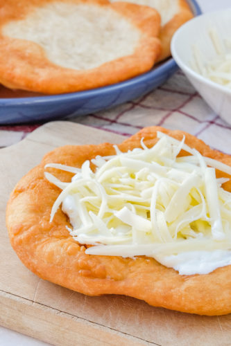 hungarian Lángos with cream and cheese on top on wooden board