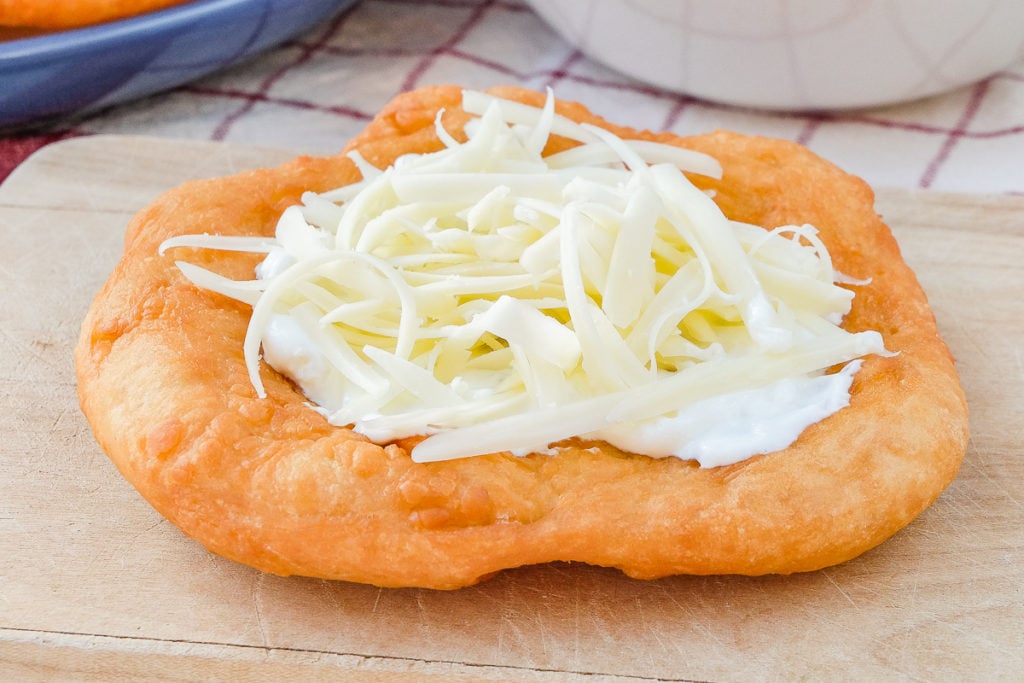 hungarian fried bread with shredded cheese and cream on top on wooden board