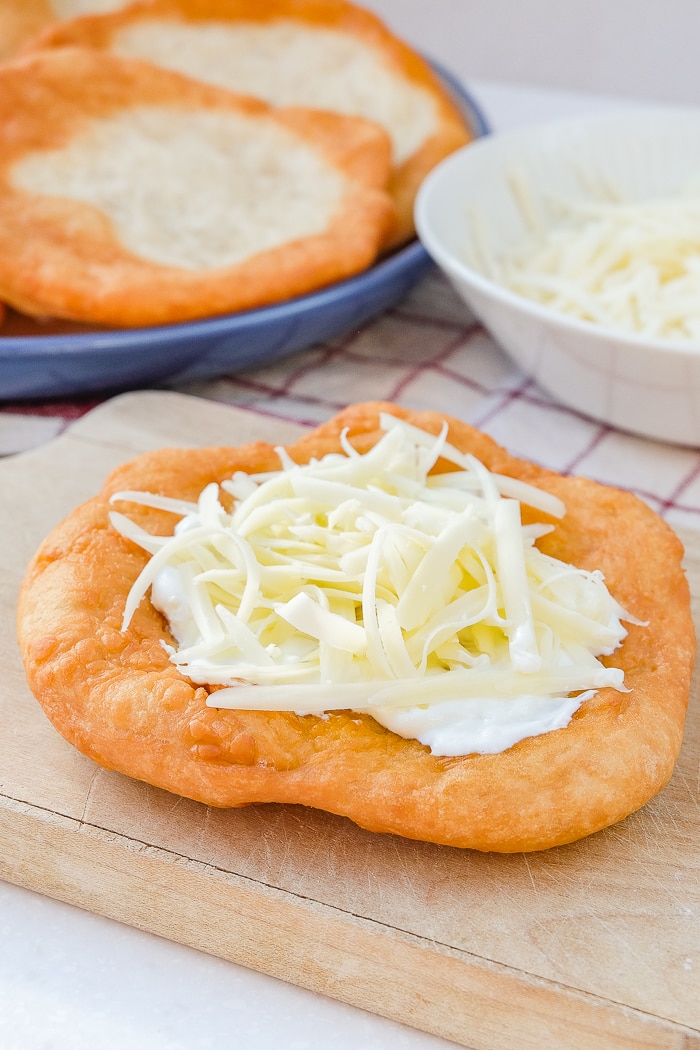 hungarian langos with shredded cheese on top on wood with more langos behind